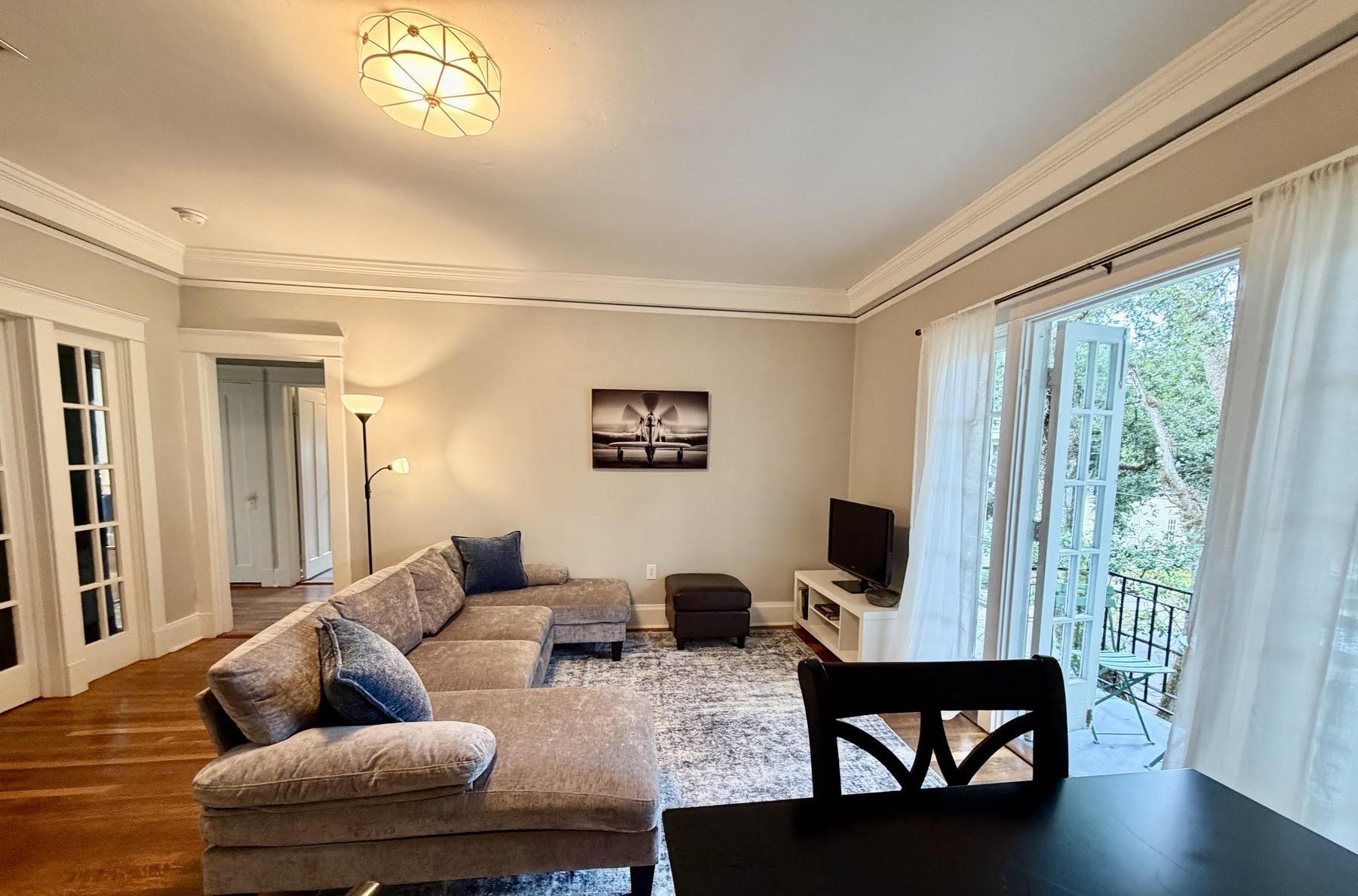 Living room in Apartment D with a grey corduroy sectional sofa and French doors open to the balcony